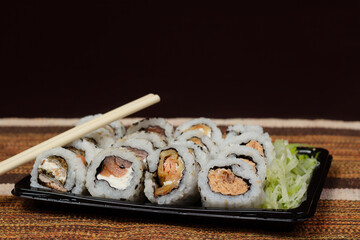 Pieces of sushis, uramaki, with cucumber salad aside and a pair of hashi, on black plastic plate