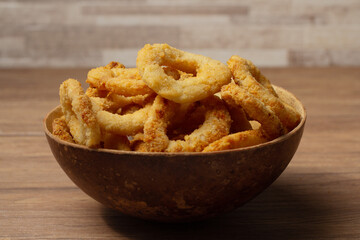 Onion rings in brown bowl on wooden table 