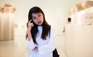 Fototapeta premium Thoughtful chinese woman visitor in the historical museum looking at art object