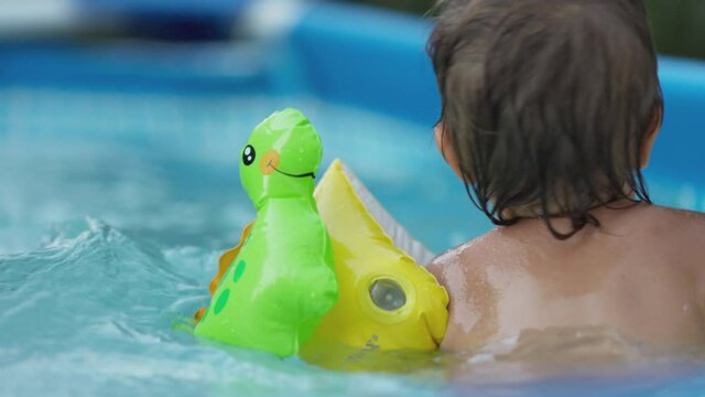 Kid in oversleeves swims in the pool in the yard