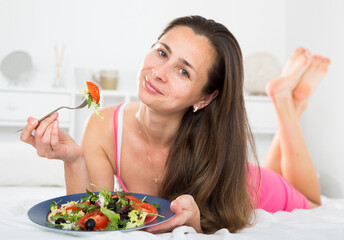 Woman eating an appetizing salad in bed. High quality photo