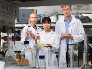 Modern male and female scientists in white coats posing at biochemical laboratory