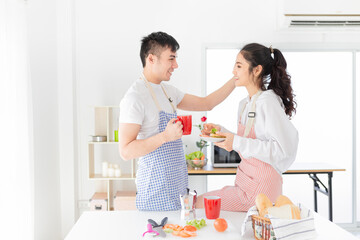 Obraz na płótnie Canvas asian man and asian woman eating meal in the morning, they have breakfast in kitchen room, he holding hot coffee cup, she holding sandwich with hand, they feeling happy and smile, happiness honeymoon 