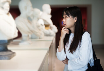 Fototapeta premium Chinese girl with interest looking around at ancient sculptures in museum