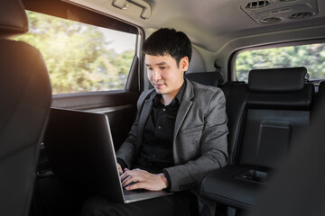 business man using laptop computer while sitting in the back seat of car