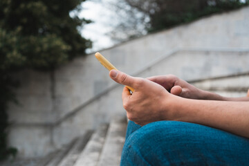 Closeup of the male hands using his smartphone sitting on the stair outside