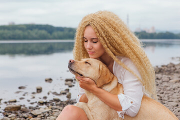 Young woman huging with her labrador retriever dog on the river shore