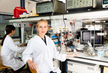 Portrait of glad cheerful smiling young female scientist near laboratory equipment at biochemical lab