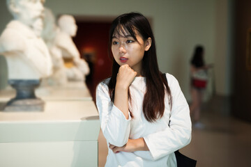 Attentive chinese girl with interest looking around at ancient sculptures in gallery