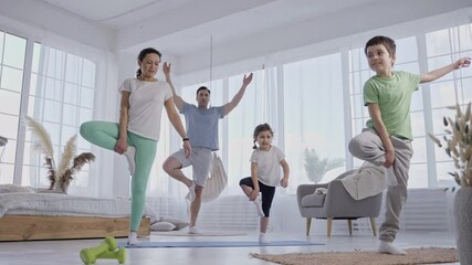 Healthy family with preteen kids keeping balance in tree pose while practicing yoga at home. Active parents teaching little children to do yoga exercises, sports lifestyle, bonding leisure activity