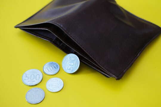Indonesia rupiah coins spread from inside of wallet over yellow background