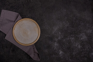 An empty beige ceramic plate on a dark black background. Grey linen napkin.