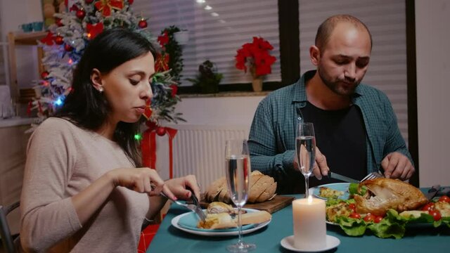 Man and woman clinking glasses of champagne at festive dinner, celebrating christmas eve with chicken and alcohol. Couple enjoying meal for traditional holiday celebration. People eating