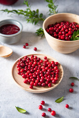 juicy forest lingonberry with a branch in a wooden bowl on white table with jam. Concept homemade healthy food. Close up