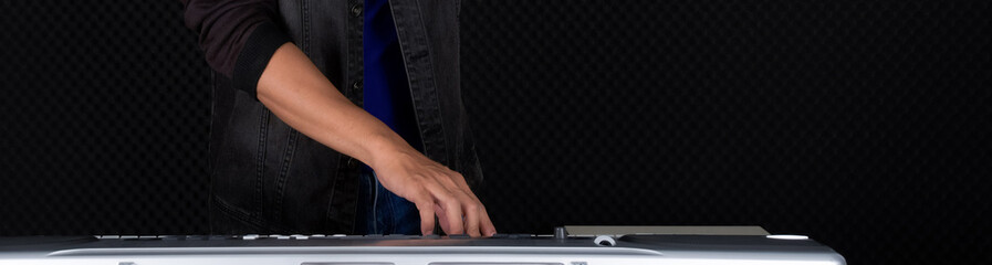 Closeup musician's hand playing on a music keyboard player in front of black soundproofing walls. Musician producing music in professional recording studio.