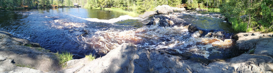 Naklejka premium Panorama of a bubbling waterfall with brown water on the Tokhmayoki River in Karelia from an ecological trail.