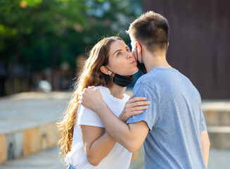Fototapeta premium Young man and girl in masks are hugging and kissing each other in cheek