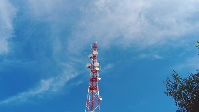 Large red and white pole with big cellular antennas and telecommunications radars day time upview with blue sky and airy white clouds on background