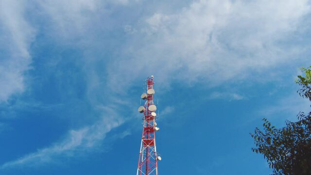 Large red and white pole with big cellular antennas and telecommunications radars day time upview with blue sky and airy white clouds on background