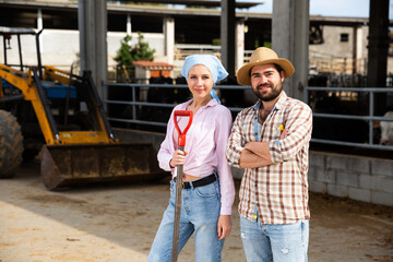 Confident young man and woman owners of dairy farm standing near tractor outdoors