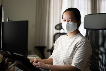 Fototapeta na wymiar Asian woman with protection mask is working at home looking at camera 