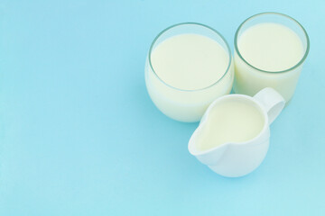 Milk in glasses and white jug on blue background, room for text.	