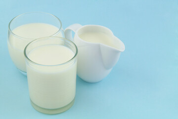 Jug with milk and two glasses of milk on blue background.	