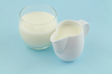 Milk or cream in jug and glass on blue background