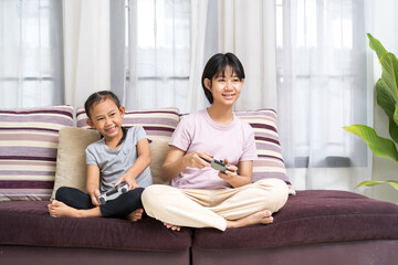 Happy Asian girl with sister playing video game using joystick or controller while lying on the floor at home