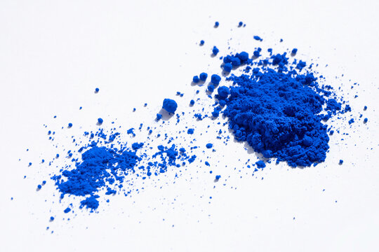 Close up of a large and a small portion of ultramarine, cobalt or indigo blue pigment isolated on white. The pigment was mixed with linseed oil to make oil paint. Narrow depth of field