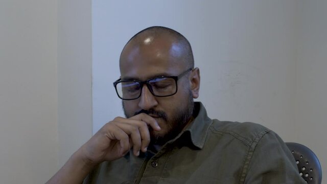 Ethnic Minority Bald Male With Eyewear, Hand On Chin, Swivelling On Chair Thinking. Static