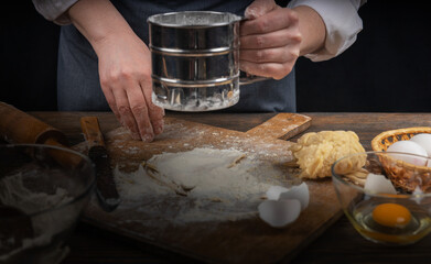 Women's hands, flour and dough. A woman in an apron cooking dough for homemade baking, a rustic home cozy atmosphere, a dark background with unusual lighting.