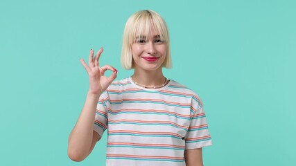 Smiling happy cheerful amazing young blonde short haircut woman 20s years old wears striped t-shirt showing okay ok zero fingers gesture isolated on pastel plain light blue background studio portrait