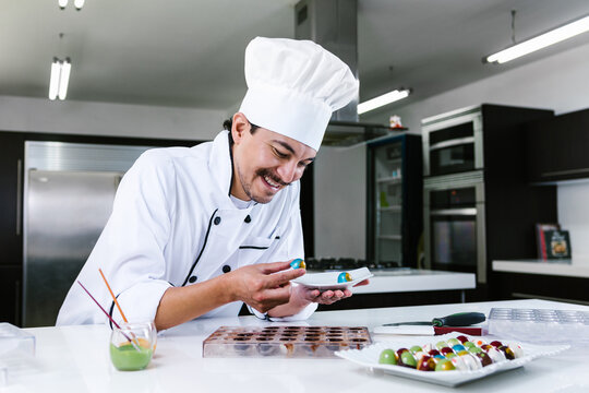 young latin man chocolatier in chef hat standing with chocolates candies on plate in a commercial kitchen in Mexico Latin America