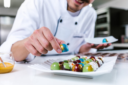 young latin man chocolatier in chef hat standing with chocolates candies on plate in a commercial kitchen in Mexico Latin America