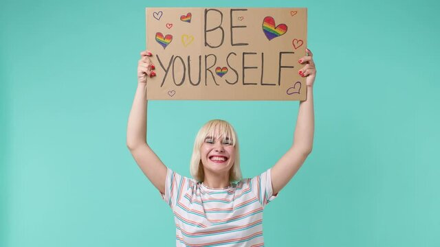 Happy young blonde short haircut woman 20s years old wear striped t-shirt hold raise poster billboard be yourself above head scream shout isolated on pastel plain light blue background studio portrait