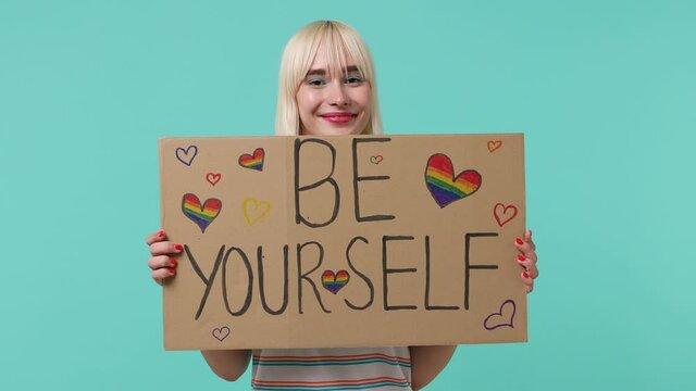Smiling happy stunning vivid young blonde short haircut woman 20s years old wears striped t-shirt hold raise poster billboard be yourself isolated on pastel plain light blue background studio portrait