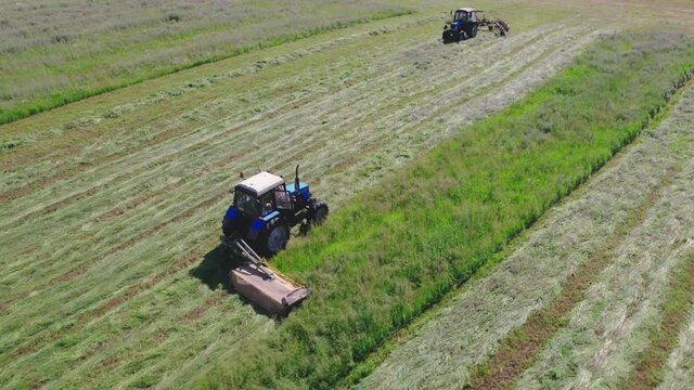 Aerial view of two tractors mowing and raking grass in the field in summer. Agricultural machines moving towards each other. Concept of seasonal hay harvesting