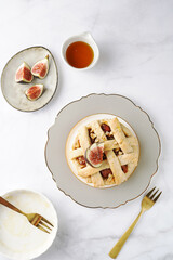 A sweet fig tart pastry on a sophisticated plate, two golden dessert spoons, honey, cut figs on a marble surface, top view