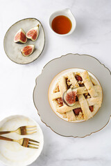 A sweet fig tart pastry on a sophisticated plate, two golden dessert spoons, honey, cut figs on a marble surface, top view