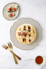 A sweet fig tart pastry on a sophisticated plate, two golden dessert spoons, honey, cut figs on a marble surface, top view