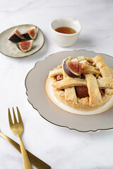 A sweet fig tart pastry on a sophisticated plate, two golden dessert spoons, honey, cut figs on a marble surface