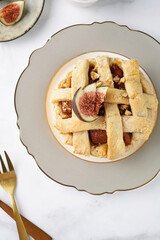 A sweet fig tart pastry on a sophisticated plate, two golden dessert spoons, honey, cut figs on a marble surface, top view