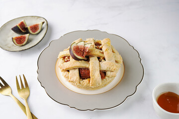 A sweet fig tart pastry on a sophisticated plate, two golden dessert spoons, honey, cut figs on a marble surface