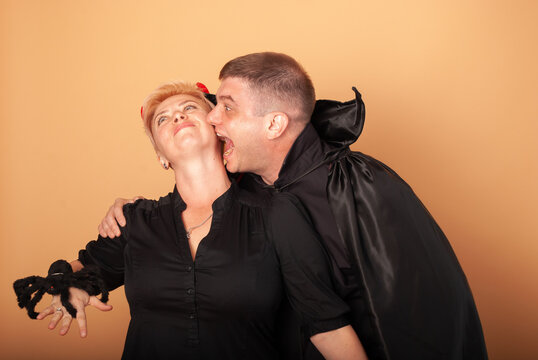 a man and a woman in the form of Count Dracula vampire and vampire witches depict biting in the neck on a beige background on Halloween