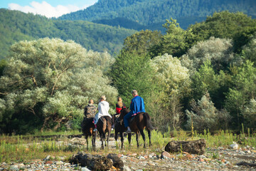 A group of people from children and adults ride horses in the mountains