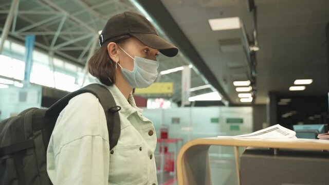 A Woman In A Mask And With A Backpack Behind Her Back Near The Check-in Desk To Board The Aircraft. Checking Passports At The Airport, Registration.