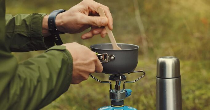 preparing food outdoors on gas burner. stir the porridge. camping cooking equipment