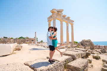 A loving couple of travelers pose with a view of the ruins of the ancient Roman temple of Apollo. Side, Tourism and tours in Turkey.