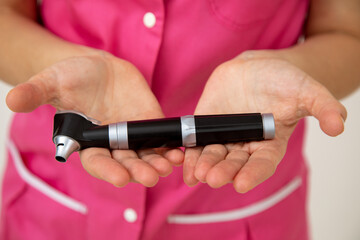 Female doctor in pink medical clothes holds otoscope in her hands . Medical research. Preventive examinations Medicine and insurance. Health protection